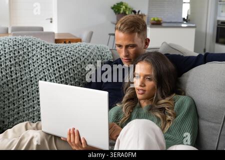 Diverse Paare sitzen auf grauem Sofa und schauen sich zu Hause einen silbernen Laptop an, einen dicken Überwurf Stockfoto
