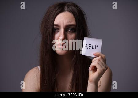 Menschenhandel. Verzweifelte Frau, die Papier hält, mit Worthilfe auf grauem Hintergrund Stockfoto