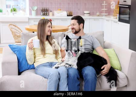 Glückliches Paar trinkt Kaffee und ruht sich mit seinem Hund zu Hause auf dem Sofa aus Stockfoto