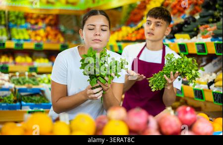 Bezweifelte junge Kundin, die beim Kauf von Grüns im Supermarkt um Rat von einem männlichen Markthelfer bittet Stockfoto