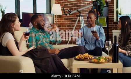 Afroamerikanerin erzählt Geschichten, während Freunde leckere Leckereien im Wohnzimmer genießen, sich unterhalten und lustige Geschichten auf einer Apartmentparty teilen, gemeinsam Brunch trinken und Snacks essen. Stockfoto