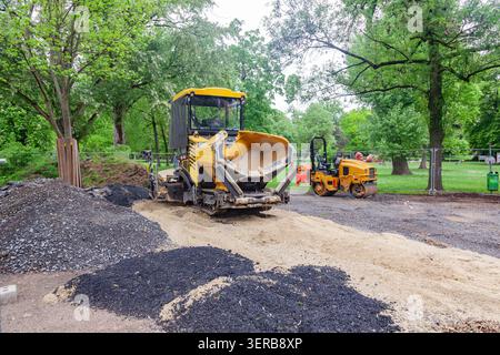 Asphaltfertiger und Straßenrollenmaschinen auf einer Baustelle in einem Park umgeben von grünen Bäumen Stockfoto