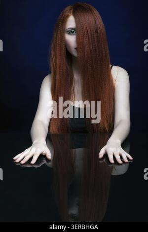 Schöne erschreckende junge Frau mit Ingwerhaar über Spiegelspiegel auf blauem Hintergrund Stockfoto