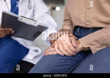 Reife Patientin lernt schlechte Diagnose von junger afrikanischer Ärztin Stockfoto
