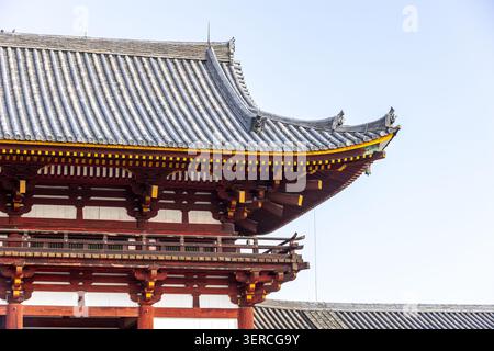 Blick auf das verzierte Ziegeldach und die rote Holzarchitektur eines traditionellen japanischen Tempels vor einem klaren Himmel in Nara, Nara, Japan. Stockfoto