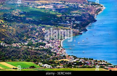Aus der Vogelperspektive auf Saint Pierre Stadt und Bucht in Martinique, mit üppigen Bergen, einem Küstendorf und Booten im blauen Karibischen Meer. Stockfoto