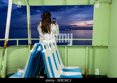 Eine junge Frau fotografiert den Sonnenuntergang über der Lagune von Venedig vom Deck einer Fähre aus Venedig, Italien Stockfoto