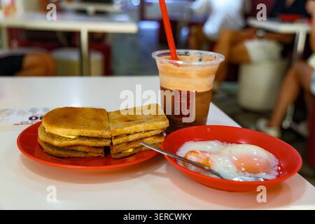 Traditionelles singapurisches Frühstück mit Kaya-Toast, weich gekochten Eiern und Eiskaffee, serviert in einem Café im Kampong Glam District von Singapur. Stockfoto