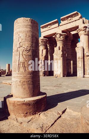 Blick auf den antiken Tempel des Horus mit detaillierten Hieroglyphenschnitzereien auf einer Steinsäule und massiven Säulen unter einem klaren blauen Himmel in Edfu, Assuan Go Stockfoto