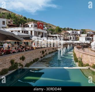 Konya, Türkei - 8. Juni 2025: Kanal im Dorf Sille mit Brunnen, Restaurants in Cafés im Freien, traditionellen weißen Gebäuden und einer türkischen Flagge Stockfoto