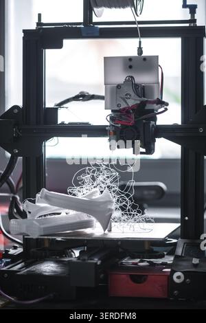 3D-Drucker funktioniert, wodurch bei teilweise geformten Modellen ein verworrenes weißes Kunststofffilament auf der Bauplatte entsteht, das einen technischen Fehler oder Fehler veranschaulicht Stockfoto