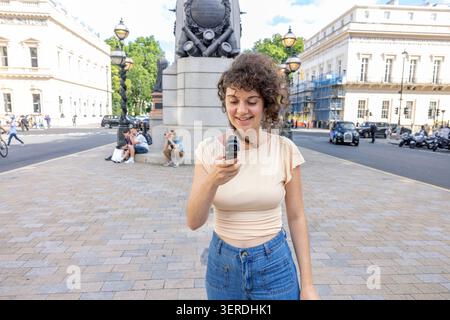 Eine lächelnde junge Frau, die eine DJI Osmo Pocket-Handkamera benutzt, in einer Londoner Straße, London, Großbritannien. Stockfoto