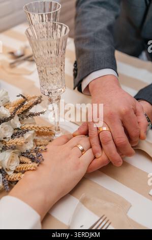 Eine zarte Nahaufnahme eines frisch vermählten Paares, das Hände hält und ihre goldenen Eheringe zeigt. Stockfoto