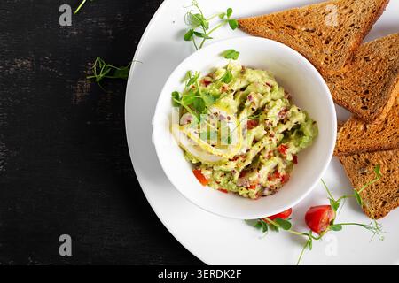 Frische Guacamole mit Zitrone und Vollkorntoast auf weißer Platte Stockfoto