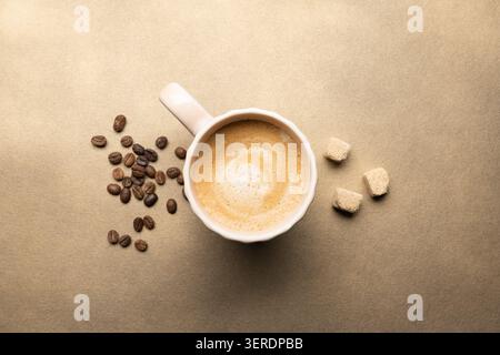 Kaffee mit Milchschaum, Kaffeebohnen und Zuckerwürfeln auf beigefarbenem Hintergrund Stockfoto