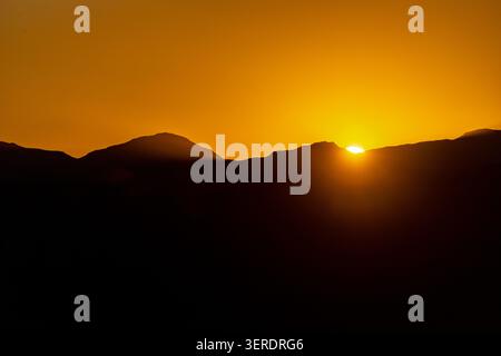 Blick auf den Sonnenuntergang hinter den Silhouetten der Berggipfel unter dem leuchtenden orangefarbenen Himmel Mazenod, Maseru, Lesotho. Stockfoto