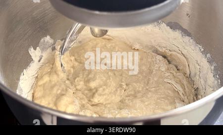 Teigmischung in einer Edelstahlschale, die mit einem Standmixer zubereitet wird, wobei Mehl und feuchte Zutaten zum Backen miteinander vermischt werden Stockfoto
