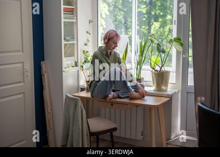 Glückliche, reife Frau in Kopfhörern, die Musik-Playlist im Online-Audio-Streaming-Dienst scrollen. Stockfoto