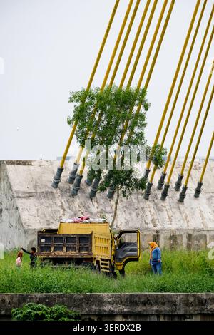 Pekanbaru, Indonesien - 28. September 2025: Einheimische stehen neben einem gelben Nutzfahrzeug in der Nähe einer riesigen modernen Brückenbauinfrastruktur Stockfoto