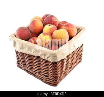 Pfirsiche in einem quadratischen Korb mit beigefarbenem Stoffbezug. Weißer Hintergrund. Stockfoto