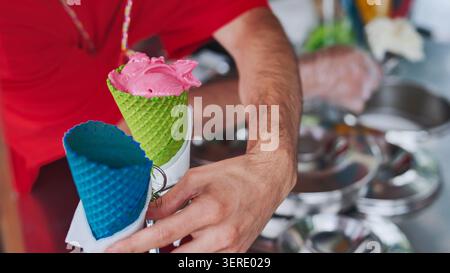 Ein Eisverkäufer schöpft Eis in bunte Waffelkegel. Stockfoto