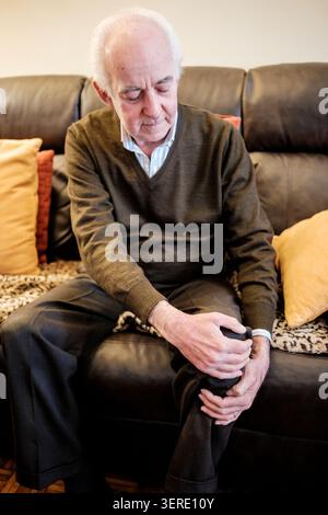 Ein älterer Mann, der an Knieschmerzen leidet und sein Bein hält Stockfoto