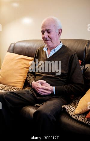 Ein älterer Mann sitzt auf einem Sofa, hält seinen schmerzhaften Magen, während er Verdauungsstörungen hat Stockfoto