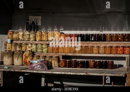 Zahlreiche Glasgläser mit einer lebhaften Auswahl an hausgemachtem eingelegtem Gemüse und süßen Obstkonserven werden akribisch auf rustikalem Woo ausgestellt Stockfoto