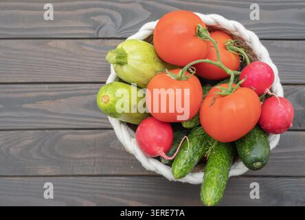 Frisches Gemüse im Korb mit Tomaten, Gurken, Radieschen, Zucchini und Dill auf hölzernem Hintergrund. Stockfoto