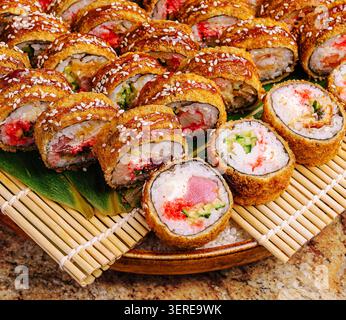 Eine Vielzahl von Sushi-Brötchen wird ordentlich auf einer Holzplatte mit Bambusmatte darunter gelegt. Die farbenfrohen Rollen sind mit verschiedenen Zutaten und Texturen versehen und sorgen so für eine verlockende Präsentation. Stockfoto