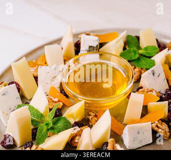 Eine Käse- und Obstplatte ist auf einem runden Teller angeordnet. Verschiedene Käsesorten werden in kleine Stücke geschnitten. Es gibt Nüsse und getrocknete Früchte rund um den Käse. Stockfoto
