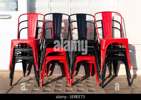 An einem sonnigen Nachmittag stapeln sich die Stühle in Rot und Schwarz ordentlich am Eingang eines Cafés in Lytham St Annes, England. Stockfoto