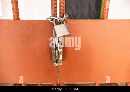 Eine horizontale Makroansicht mit Fokus auf ein starkes Sicherheitsvorhängeschloss aus silbernem Metall, das fest an einem schweren Verriegelungsmechanismus eines orange lackierten Metallprisos befestigt ist Stockfoto