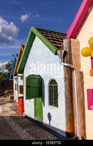 Eine vertikale Perspektive, fokussiert auf ein malerisches kleines weißes Häuschen mit einem hellgrünen Fenster und offenen Fensterläden, Teil einer farbenfrohen alle Stockfoto