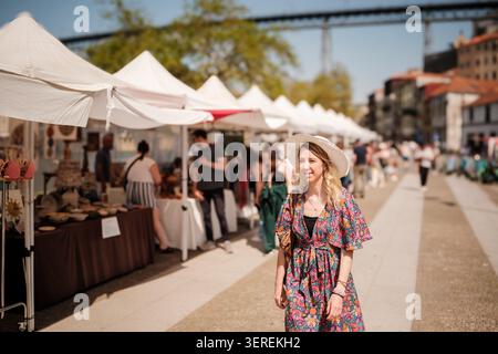 Frau mit Sonnenhut lächelt beim Spaziergang durch einen Kunsthandwerksmarkt Stockfoto