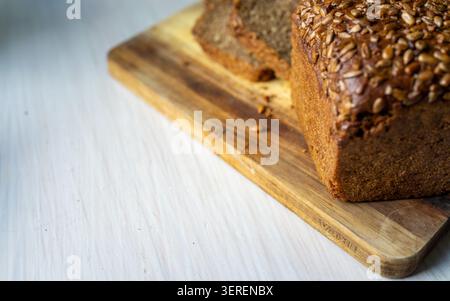 Nahaufnahme von dichtem Vollkornbrot, belegt mit gemischten Samen auf rustikalem Holzschneidebrett, mit zwei dicken Scheiben geschnitten und Krümel auf p Stockfoto