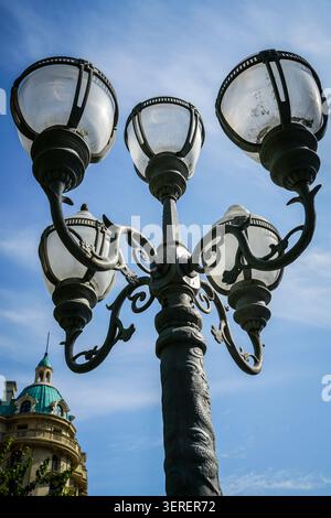 Eine flache, nach oben gerichtete Straßenleuchte aus schwarzem Gusseisen mit fünf Glaskugeln und dekorativem Scrollwerk vor einer Vibran Stockfoto