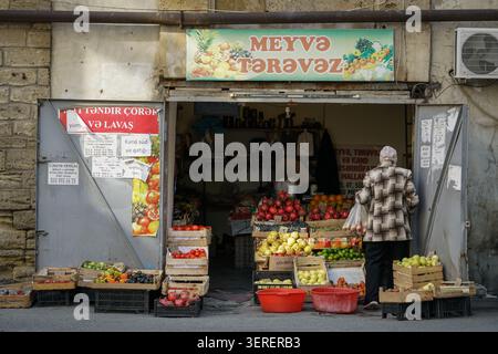 Eine Person, die eine karierte Jacke trägt, geht zu einem lebhaften Obst- und Gemüsestand im Freien, der mit frischen Produkten, einschließlich knallroter Pomegra, überfüllt ist Stockfoto