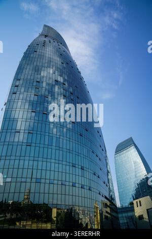 Das Bild zeigt zwei moderne, geschwungene Glashochhäuser, die als Flame Towers bekannt sind und sich zu einem hellblauen Himmel erheben. Wolken und ferne Strukturen Stockfoto