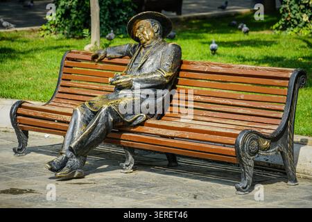 Eine Bronzestatue, die den aserbaidschanischen Schriftsteller Rustam Ibrahimbekov darstellt, wird auf einer braunen Parkbank in Baku, Aserbaidschan, gezeigt. Die Detailskulptur p Stockfoto