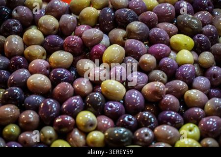 Eine lebendige Nahaufnahme eines großen Sortiments an gebratenen Oliven in verschiedenen Grün-, Violett- und Schwarztönen. Diese glitzernden Oliven A Stockfoto