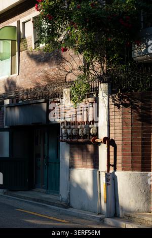 Alte koreanische Gasse mit einer alten roten Backsteinmauer und Gaszählern, die in warmes Sonnenlicht getaucht sind Stockfoto