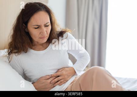 Frau, die im Bett sitzt und Bauchschmerzen hat Stockfoto