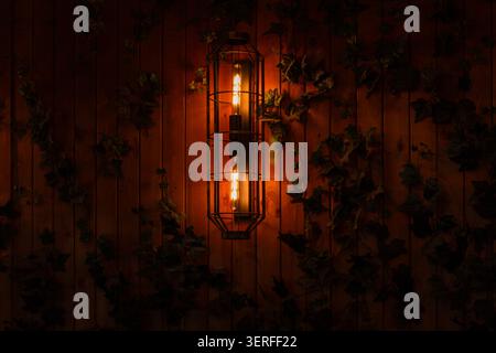Warme Vintage Wandleuchte an Holzwand mit Efefeublättern Stockfoto