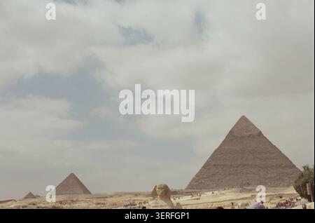 35-mm-Panoramaansicht des gesamten Gizeh-Komplexes mit der kleinen Sphinx in der unteren Mitte, flankiert von zwei großen Pyramiden und einer dritten kleineren auf Stockfoto
