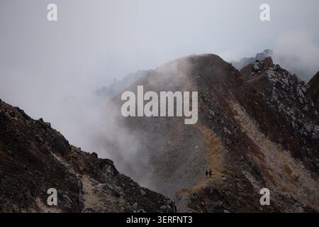 Zwei Wanderer auf dem nebeligen Felsgrat des Mount Sibayak, einem aktiven Vulkan in der Nähe von Berastagi, Nord-Sumatra, Indonesien, bei Sonnenaufgang Stockfoto