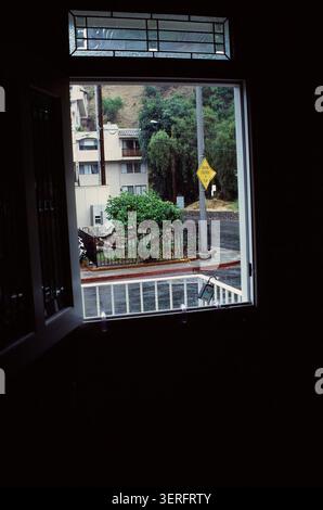 Ein Vintage-CRT-Monitor zeigt einen Blick über die Straße auf ein Stadtviertel mit Bäumen, einem Gebäude und Straßenschildern in einem verdunkelten Innenraum. Stockfoto