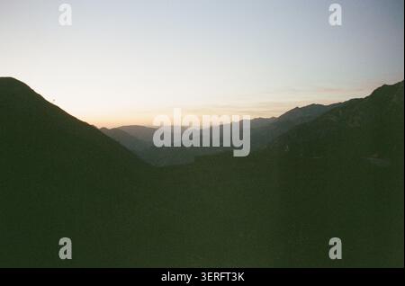 Ruhige Aussicht bei Sonnenuntergang durch einen Bergpass, der die Silhouetten in Schichten und einen warmen goldenen Horizont enthüllt. Moody, atmosphärische Landschaft erfasst Stockfoto