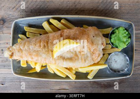 Goldener knuspriger Fisch und Chips, serviert mit pikanter Zitrone und lebhaften grünen Pilzerbsen Stockfoto