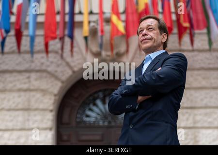 Reifer Geschäftsmann posiert mit überkreuzten Armen neben internationalen Flaggen Stockfoto